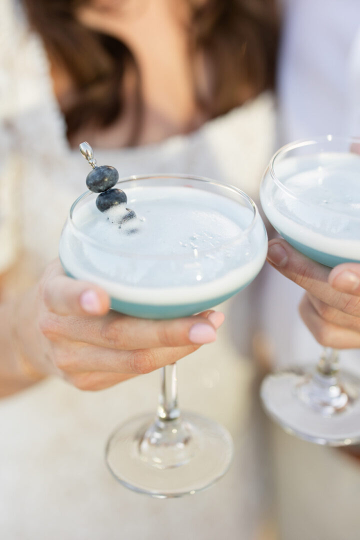 Two frothy blue cocktails garnished with blueberries